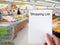 Female hand holding shopping list paper on grocery store blur ba