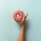 Female hand holding sweet donut over blue background. Top view, flat lay. Square crop. Weight lost, sport, fitness, diet concept.