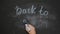 Female hand holds blue chalk and writes back to school on black chalk board