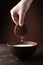 A female hand holds one chocolate chip cookie from which milk is dripping into a plate