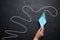 A female hand holds a paper boat against a black chalkboard background with a long path. Concept of mentorship and assistance