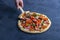 Female hand holds pizza with culinary shovel. Fresh prepared pepperoni pizza with salami and cheese on a dark background. Italian