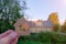 female hand holds a small toy wooden house. In the background is a real residential building. horizontal photo. Idea - a