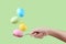 Female hand holds a spoon on which multi-colored eggs are balanced, on a green background. Unusual design, Easter concept, copy