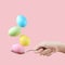 Female hand holds a spoon on which multi-colored eggs are balanced, on a pink background. Unusual design, Easter concept, copy