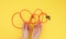 Female hand holds twisted cable for charging mobile devices in a red textile wrapper on a yellow background