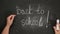 Female hand holds white chalk and writes back to school on black chalk board