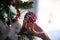 Female hand with holiday manicure holding shiny red holiday bauble hanging from a christmas tree