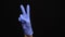 Female hand in a latex medical glove makes an peace gesture isolated on black background