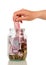 Female hand is laying money bills in glass jar, isolated on whit