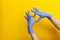 Female hand in lilac glove, fingers folded into a heart sign on yellow background