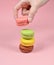 Female hand lowers the pink macaroons cookies. A stack of macaroons on a pink pastel background.