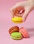 Female hand lowers the yellow macaroons cookies. Many macaroons on a pink pastel background. Minimalism.