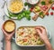 Female hand making pasta casserole with tomato, bacon and cheese, top view.