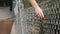 Female hand moving along the surface of grid. Arm of young woman touching metal wire fence. Girl walking during summer