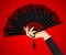 Female hand with open black vintage fan on red light ba