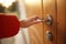 A female hand opens a brown wooden door by clicking on a chromed handle