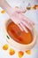 Female hand orange paraffin wax in bowl. Manicure beauty spa salon