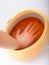 Female hand and orange paraffin wax bowl. Woman in beauty salon