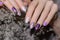 Female hand with pearly nail design. Glitter purple nail polish manicure. Woman hand with white dried flower