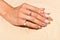 Female hand with a perfect pastel pink manicure on a pale cream-colored sand