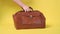 Female hand picks up and sets up old vintage travel leather suitcase on yellow background