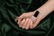 Female hand with pink nail design. Rose nail polish manicure. Woman hand hold pale red varnish on green fabric