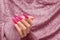 Female hand with pink stiletto nail design. Long nail polish manicure. Woman hand on glitter pink fabric background
