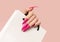 Female hand with pink stiletto nail design. Long nail polish manicure.Woman hand hold white paper bag on pink background