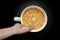 Female hand pours white pills into a white wide cup of coffee, an airplane-shaped cappuccino on a black background with vignette,