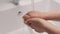 Female hand press on built-in dispenser in the sink with detergent. Woman washing dishes by yellow sponge with soap in