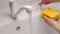 Female hand press on built-in dispenser in the sink with detergent. Woman washing dishes by yellow sponge with soap in