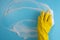Female hand in protective yellow glove, sponge and foam on blue background. House cleaning concept. Top view. Copy space