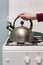 female hand puts a metal kettle on a gas burner