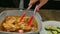 Female hand puts slices of vegetables with tongs chicken on a grill pan and pours sauce.