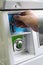 A female hand ready to insert a token into the slot of a vintage chrome coin receptacle mounted on the washing machine.