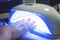 Female Hand with red nails in the lamp for manicure. Nail Lamp Dryer for Gel Nail Polish Curing Manicure Pedicure