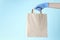 Female hand in rubber glove holding paper bag on blue background closeup