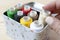 A female hand selects a bobbin with beige threads out of a box with colored threads bobbins