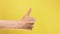Female hand show thumbs up gesture. Woman hand rise OK good sign closeup isolated at yellow screen background