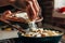 Female hand sprinkles grated cheese on a pan with pasta