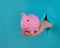 A female hand sticking out of a hole from a blue background holds a pink piggy bank.