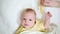 Female hand stroking  head of newborn with soft brush. Peaceful baby lying in bed and looking at camera.