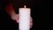 A Female Hand Takes a Burning White Candle from a Table in a Dark Room. Close up
