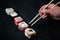 Female hand takes chopsticks sushi rolls with Chinese chopsticks. Lying on a black wooden board. View from above