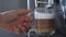 Female hand takes a glass of latte coffee coming out from an automated coffeemaker machine. Beverage drink for breakfast.