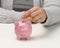 Female hand throws a coin into a pink piggy bank on a white table. Concept of accumulating cash, saving, receiving subsidies