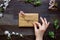 Female hand unpacking gift box wrapped with craft paper and flowers on the wooden table top view. Gift for any holiday