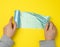 Female hand unwinds a blue plastic bag for rubbish, yellow background