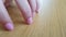 Female hand with white skin and pink short nails scratching a wooden table